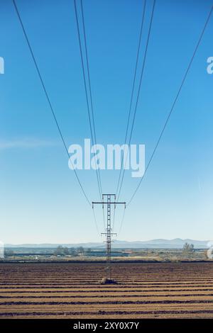 Electrical power lines stretch across a serene rural landscape under a clear blue sky, showcasing the infrastructure of power supply. Stock Photo