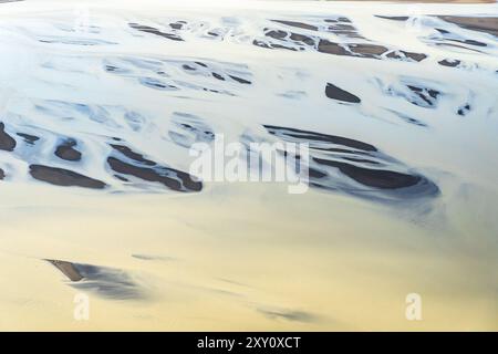 The aerial shot captures the captivating patterns formed by melting ice on a glacial river along Iceland's southern coast, showing a mix of sandy hues Stock Photo