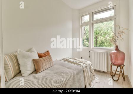 A bedroom featuring a comfortable bed with decorative pillows, a large window with a green view, and stylish vase on a wooden stool. Stock Photo