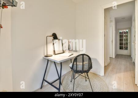 A cozy and minimalist home office corner with a sleek white desk, modern black chair, lamp, decorative vase, and empty picture frame, illuminated by n Stock Photo