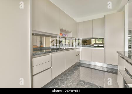 A spacious modern kitchen design featuring white cabinetry, stainless steel appliances, and granite countertops Stock Photo