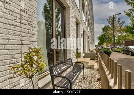 A contemporary street view showcasing a modern building with white brick walls, large windows, and sidewalk with wooden benches, and greenery. Stock Photo