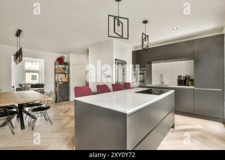 A contemporary kitchen with a central island, bar stools, and a separate dining area featuring stylish furnishings. Stock Photo