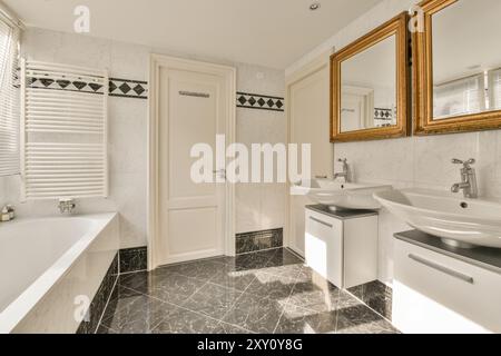 Spacious and stylish bathroom featuring white marble walls, black marble floor, a large bathtub, two sinks with mirrors, and natural light. Stock Photo