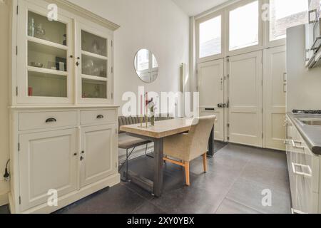 Spacious kitchen featuring a dining table, chairs, and built-in cabinets in a well-lit and contemporary setting with large windows. Stock Photo