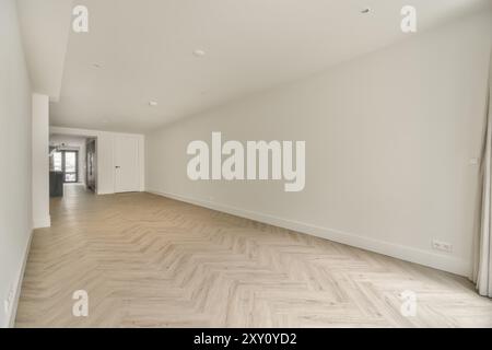 A bright, empty room with herringbone parquet flooring and white walls illuminated by natural light from a large window. Stock Photo
