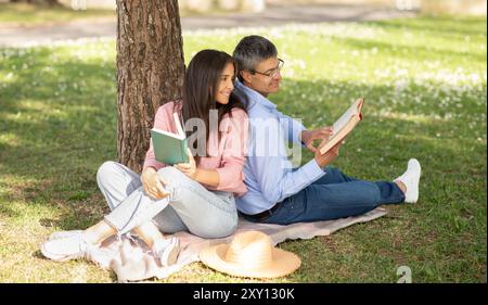 Couple enjoying relaxing afternoon under a tree while reading books Stock Photo