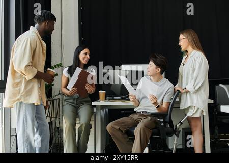 A diverse team of four works on a startup project, with one team member in a wheelchair. Stock Photo