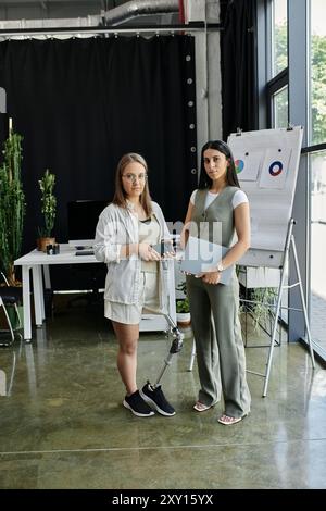 Two women stand in a modern office, collaborating on a project. Stock Photo