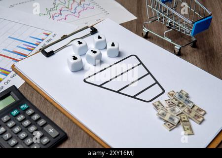 A clipboard with a sales funnel diagram and dice representing customers. Money and a shopping cart are nearby, symbolizing revenue and conversion. Stock Photo