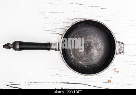 Empty old cast iron frying pan on white surface with cracked paint background Stock Photo