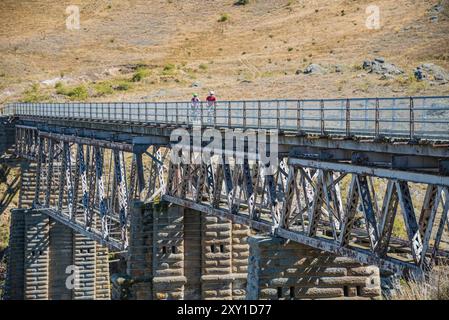 Cycling couple crossing a girder bridge on the Otago railtrail, South Island, New Zealand. Stock Photo