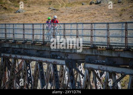 Cycling couple crossing a girder bridge on the Otago railtrail, South Island, New Zealand. Stock Photo