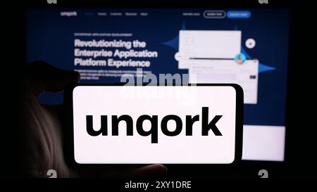 Person holding cellphone with logo of American enterprise application platform company Unqork Inc. in front of webpage. Focus on phone display. Stock Photo