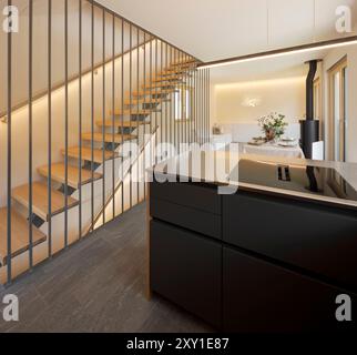 Open space with a kitchen island, a table and at the back the sofa and the stove. On the left a modern staircase in wood and metal. No one inside Stock Photo