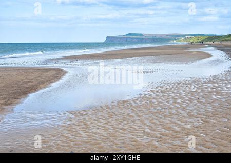 Sand ripples and pools left by the outgoing tide on Marske beach, North Yorkshire, with Saltburn town and the adjacent cliffs visible in the distance. Stock Photo