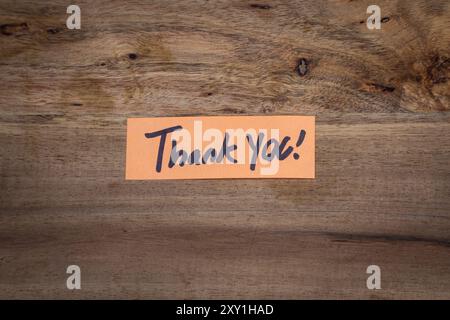 A hand written thank you note. The note is on a wooden table. Stock Photo