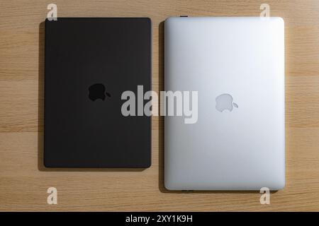 Wroclaw, Poland - March 8 2024: Old silver 15 inch Mid 2014 Macbook Pro next to new black 14 inch 2024 Macbook Pro lying on wooden table Stock Photo