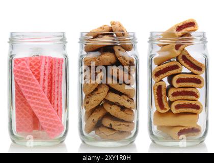 Three glass jars filled with cookies, on a white background with reflection. Jars contain, pink sugar wafers, chocolate chip and fruit bars. Stock Photo