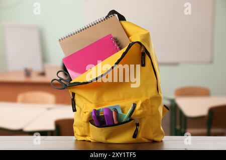 Yellow backpack with stationery on school desk in classroom Stock Photo