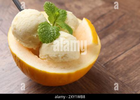 Scoops of tasty melon sorbet with mint in fresh fruit on wooden table, closeup Stock Photo