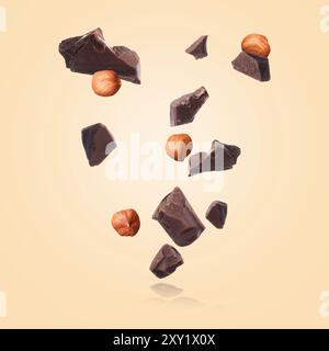 Pieces of tasty chocolate and hazelnuts falling on dark beige background Stock Photo