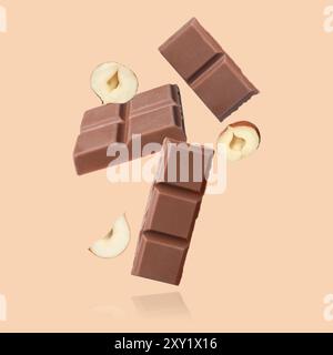 Pieces of tasty chocolate and hazelnuts falling on dark beige background Stock Photo
