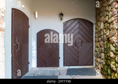Three uniquely shaped wooden doors stand before a natural stone wall, inviting exploration. Stock Photo