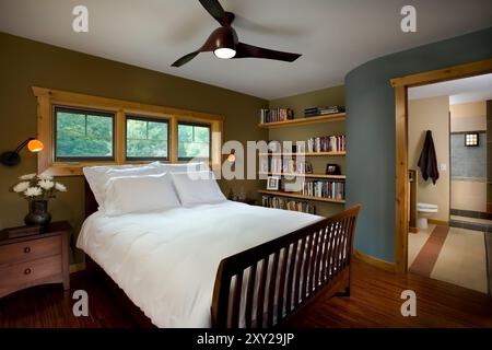 Bedroom with white bed, soft tones of olive and blue and curved entrance wall to bathroom Stock Photo