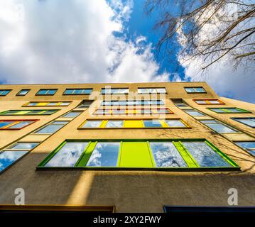 Low angle view from below of colorful window frames in a sunlit London office building under a blue sky with white clouds. Stock Photo