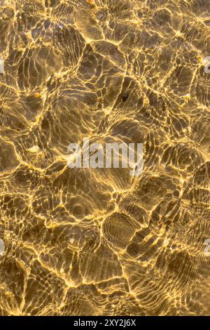 Golden ripples in shallow water creating intricate patterns. Stock Photo