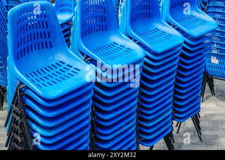 Stacked rows of blue plastic chairs with metal frames for outdoor events on town square, stackable metal framed plastic chairs Stock Photo