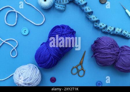 Yarn balls, measuring tape and scissors on blue background Stock Photo
