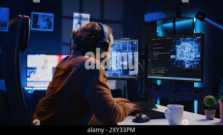 Developer updating artificial intelligence neural networks, drinking coffee and listening music in personal office. IT expert enjoying hot beverage and audio podcasts while writing AI code, camera B Stock Photo