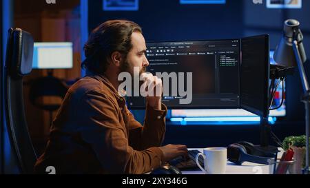 Programmer doing web development during remote job shift in neon lit home office, finishing coding project. IT specialist sitting at computer desk, working on desktop PC, camera A Stock Photo