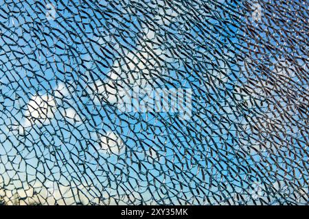 A close-up of a cracked glass surface against a backdrop of blue sky and clouds. Stock Photo