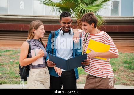 High school student smiling while showing his two colleagues the homework and lesson for the exam. Three multiracial friends reading, checking test results, and talking at the university campus. High quality photo Stock Photo