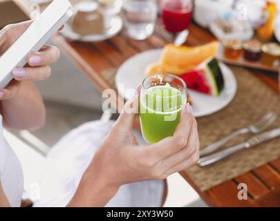 From above anonymous female enjoying green fresh drink and browsing smartphone while having healthy breakfast in morning Stock Photo