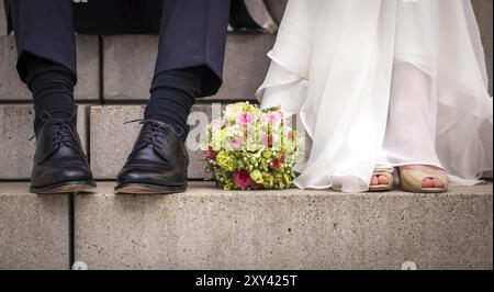 Feet of a bride and groom sitting on steps with a bouquet of flowers between them Stock Photo