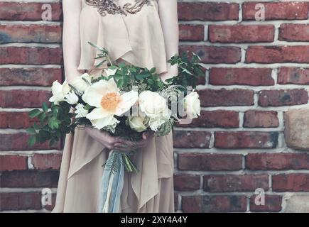 Crop woman wearing boho chic pink long dress and holding gorgeous bouquet with ribbons by the brick wall Stock Photo