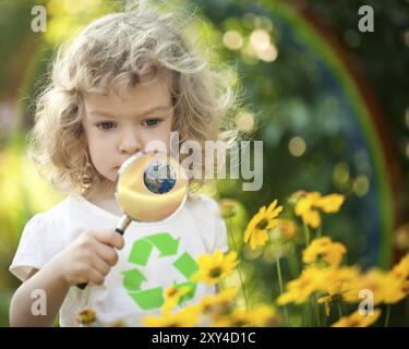 Child with recycle symbol on T-shirt looking at spring flowers against rainbow. Earth day concept. Elements of this image furnished by NASA Stock Photo