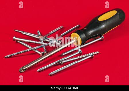 Screw driver and screws against a red background Stock Photo