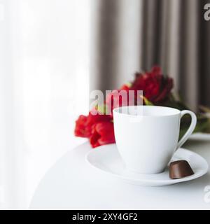 Red tulips bouquete on table, white coffee cup. Concept for greeting card for mothers day, international womans day or valentines day concept, birthda Stock Photo