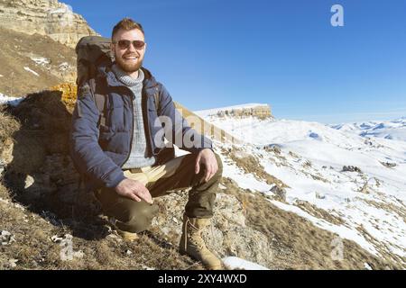 Portrait of happy laughing Hipster traveler with beard in sunglasses is sitting on nature. A man hiking in the mountains with a backpack and Scandinav Stock Photo