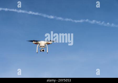 A quadrocopter with a suspended camera flies in front of a cloudless sky Stock Photo