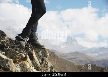 Close-up of female feet in vintage boots stand on a rock in the mountains against the background of an epic landscape of fairy-tale rocks and clouds o Stock Photo