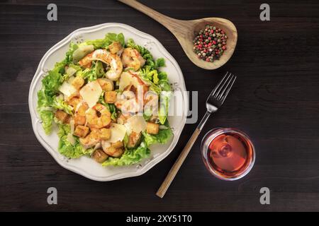 Shrimp Caesar salad with a glass of rose wine, shot from above on a dark rustic wooden background with a place for text Stock Photo