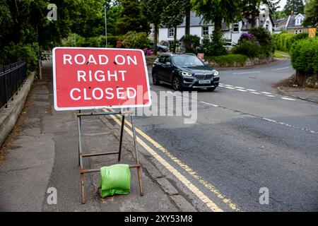 Temporary ROAD ON RIGHT CLOSED sign in the UK, a red sign with white text. It is placed on a street next to a road, weighed down with a green sandbag Stock Photo