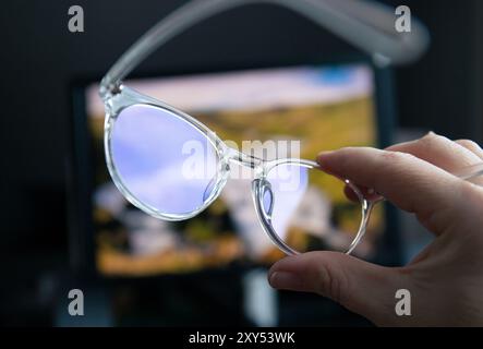 Selective focus on transparent clear blue light computer glasses and computer screen glowing on the background in home or office. Blue light glasses. Stock Photo