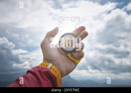 Male hand is holding a magnetic compass on the background of sky with clouds. The concept of traveling and finding your life path Stock Photo